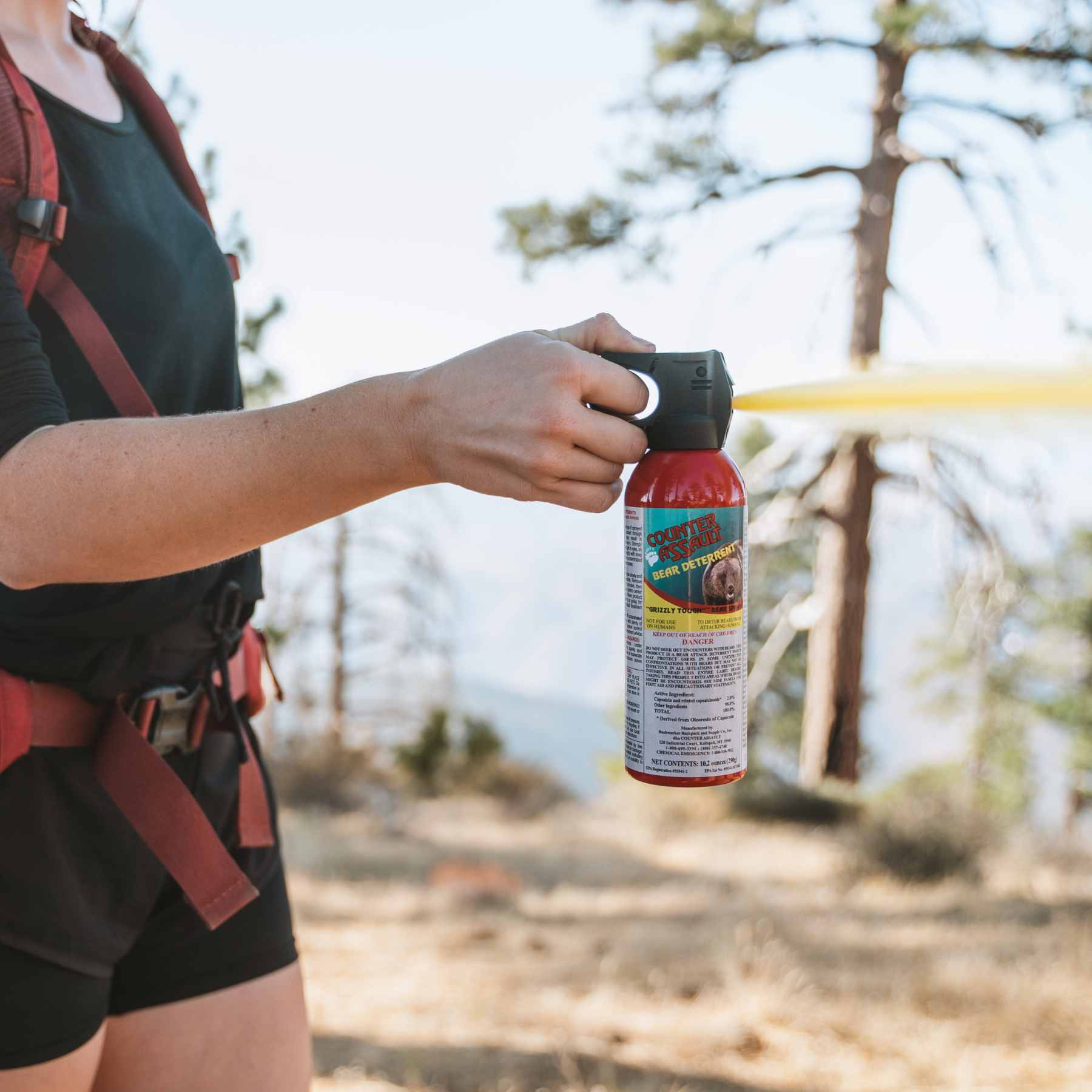 Person spraying 10.2 oz bear spray in the outdoors with red backpack on