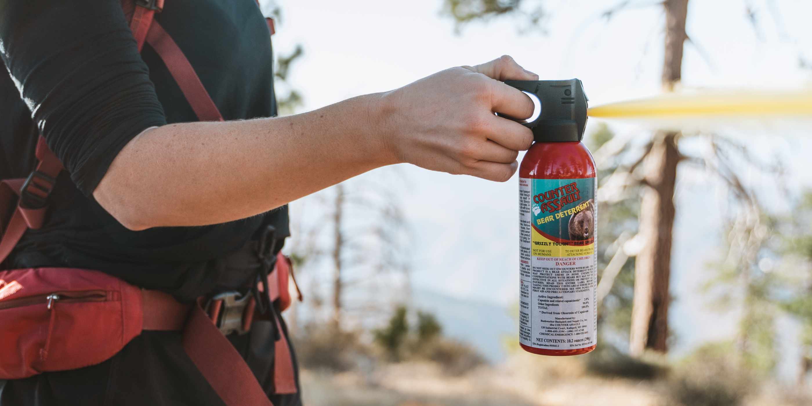 Person spraying 10.2 oz bear spray in the outdoors with red backpack on