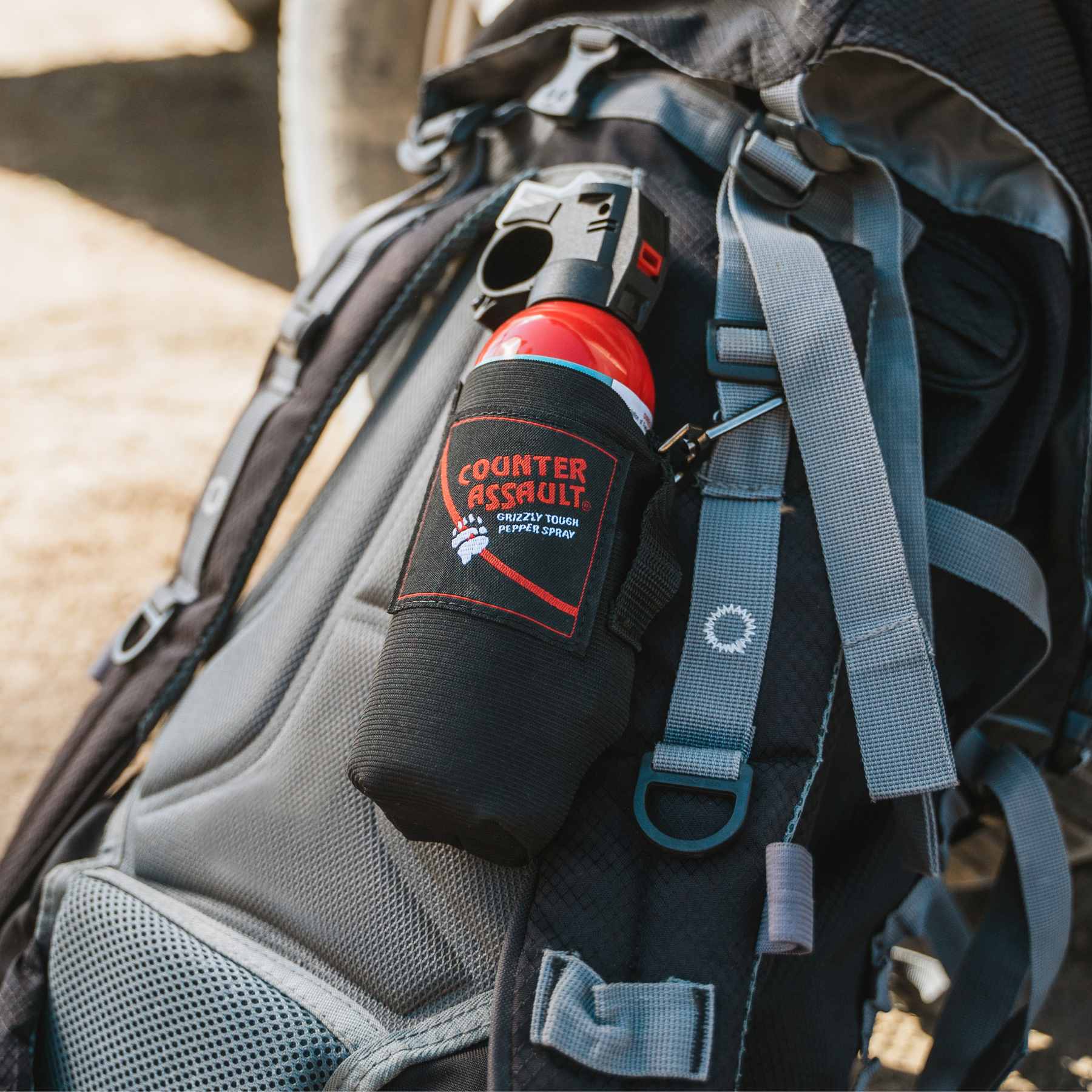 Bear spray in holster on top of blue backpack leaning on truck tire