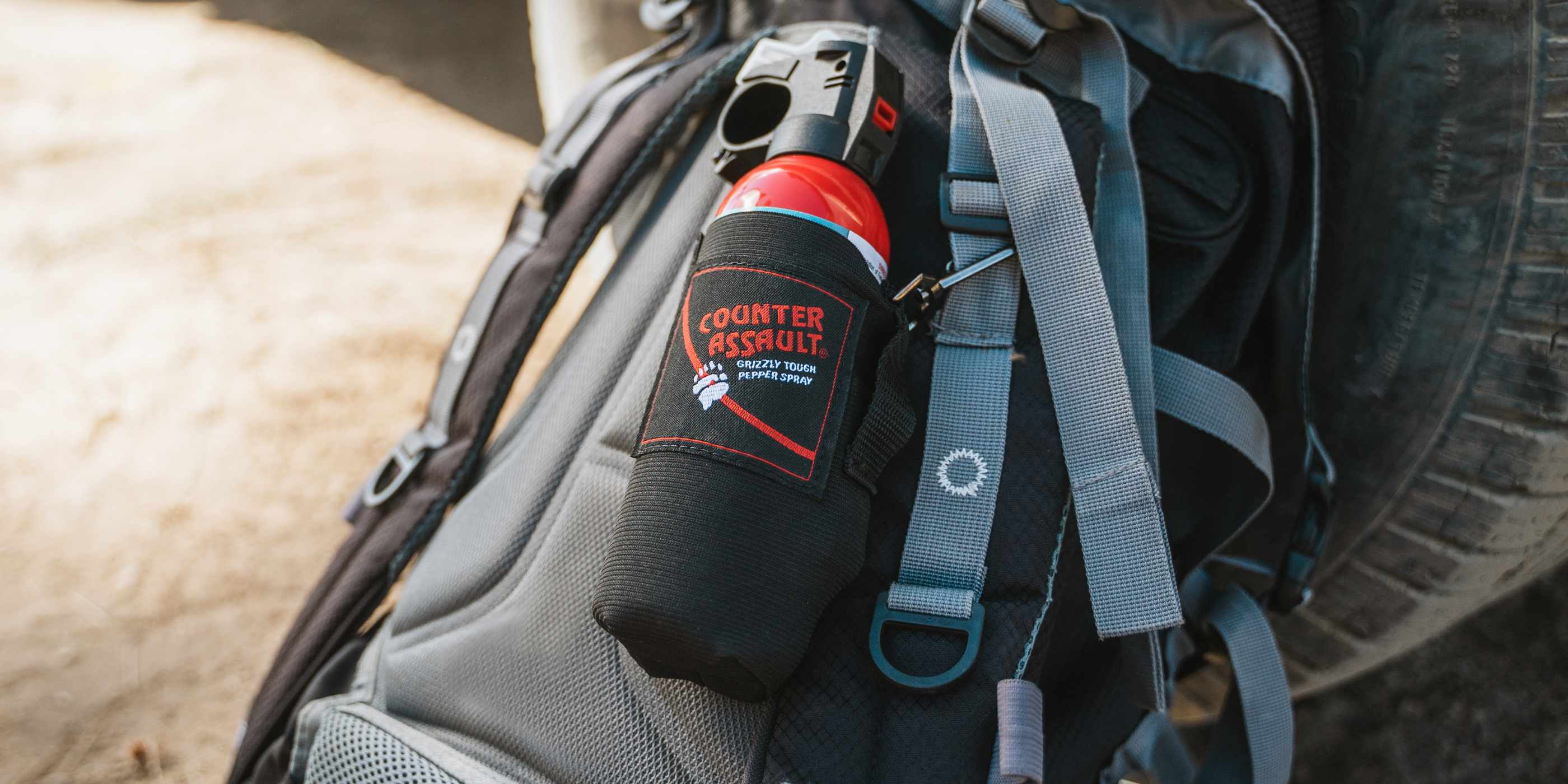 Bear spray in holster on top of blue backpack leaning on truck tire