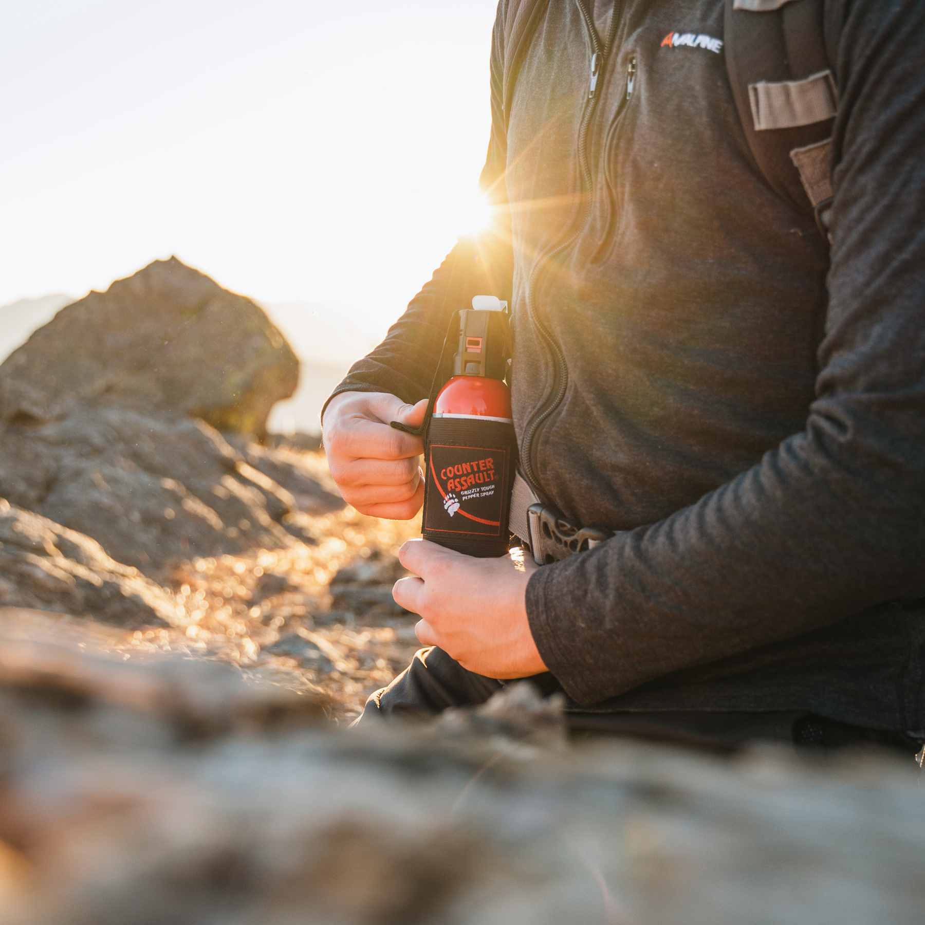 Person pulling bear spray from holster in front of rocky area
