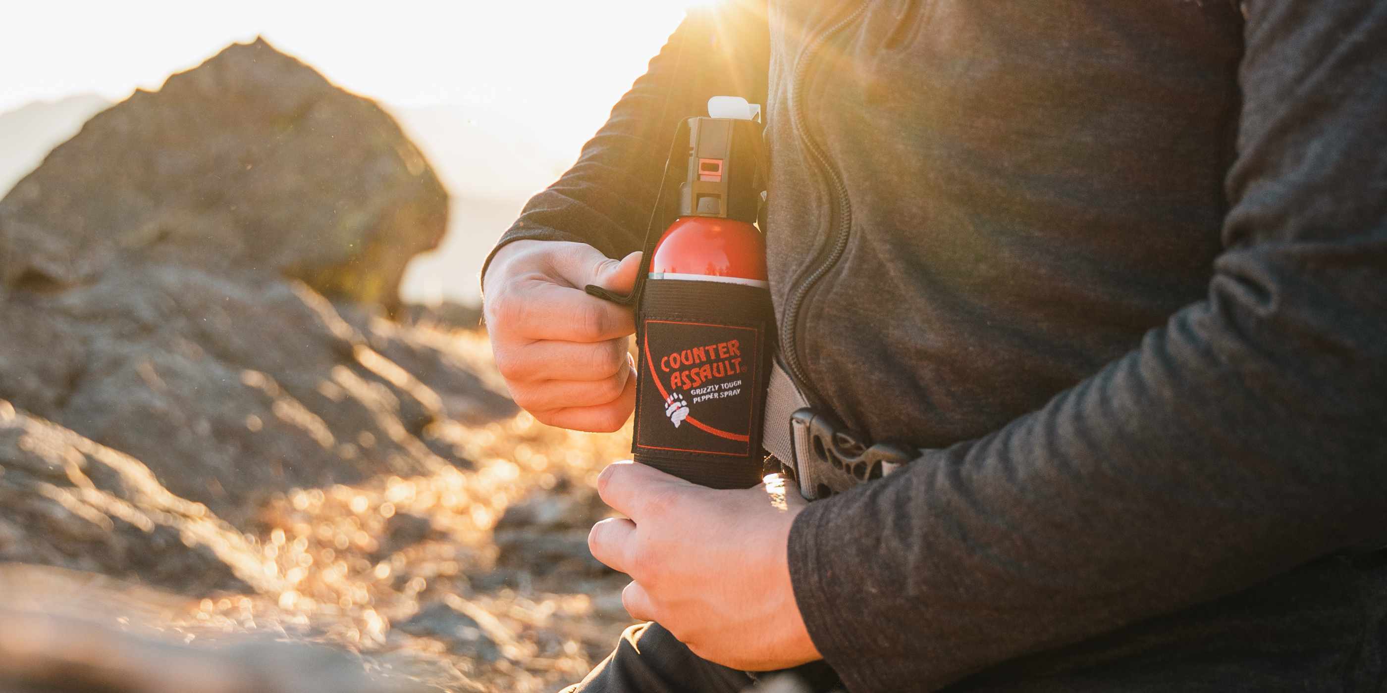 Person pulling bear spray from holster in front of rocky area