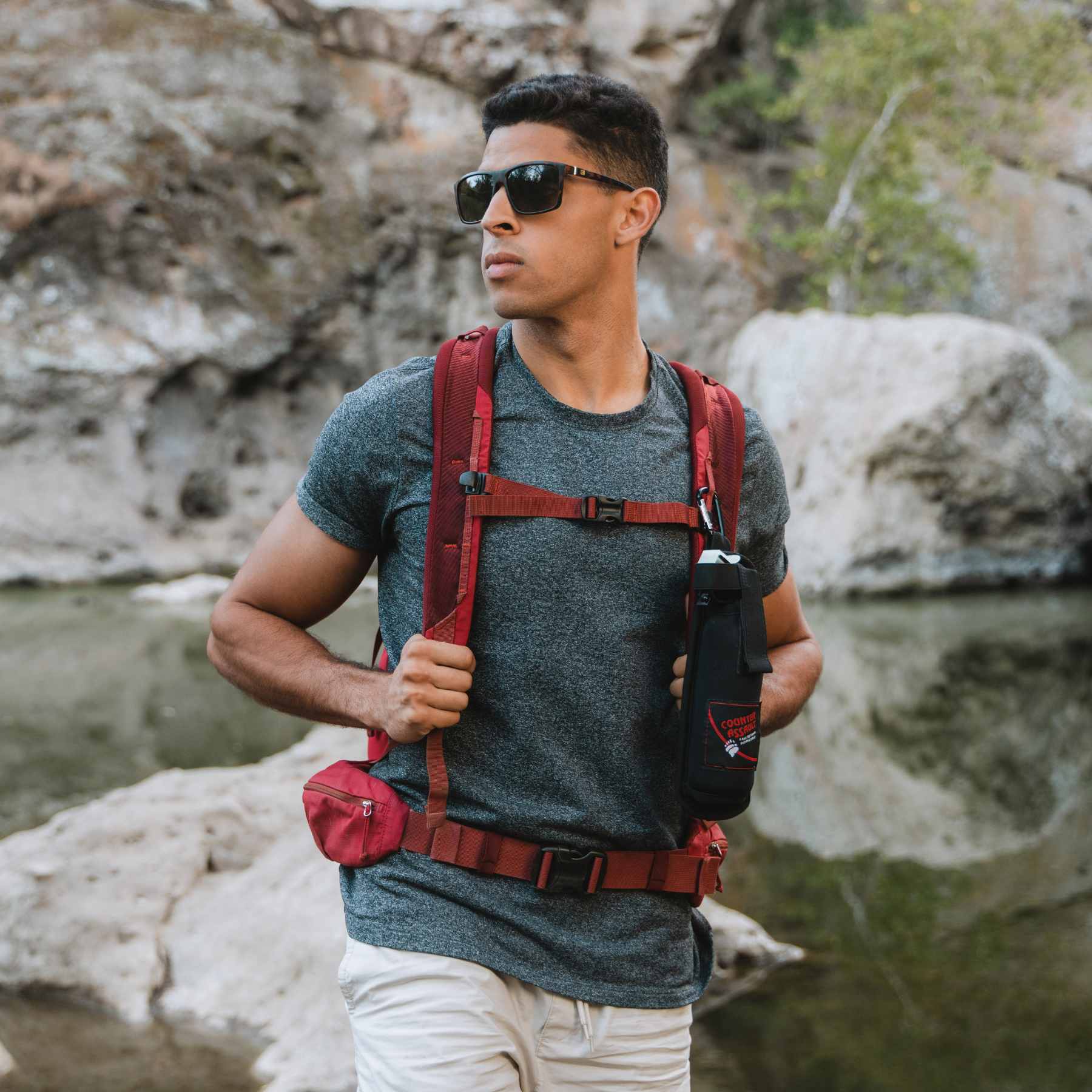 Man with bear spray in Backpack Holster attached to red backpack in front of water