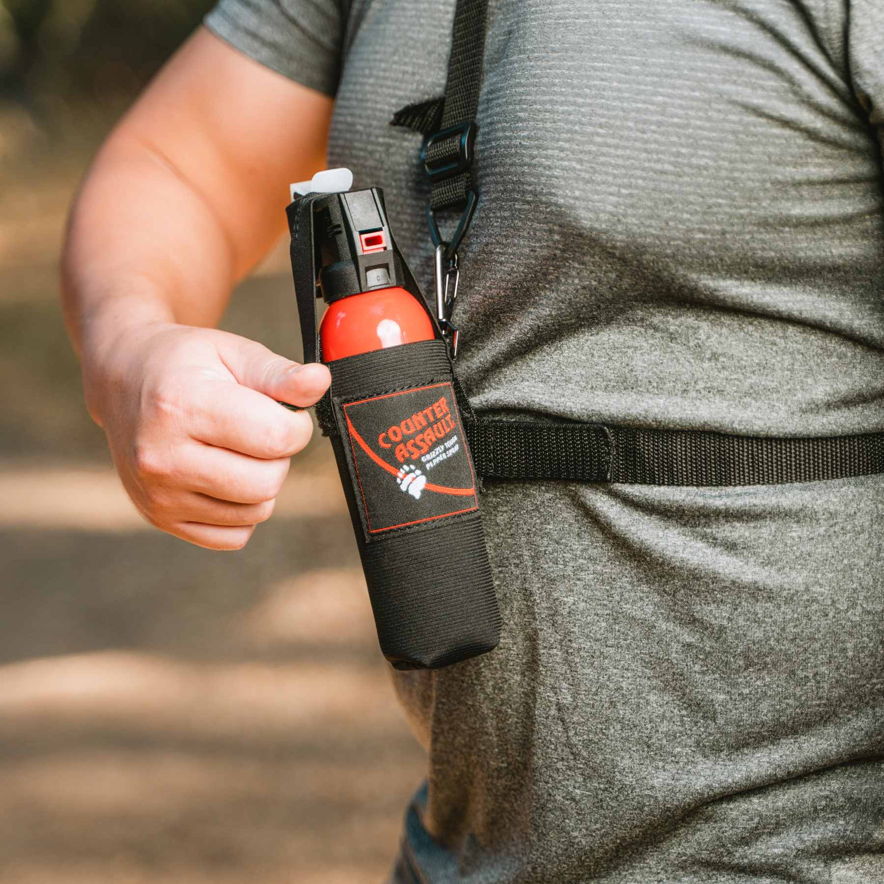 Man in gray shirt attaching Chest Holster with bear spray in it to front of body