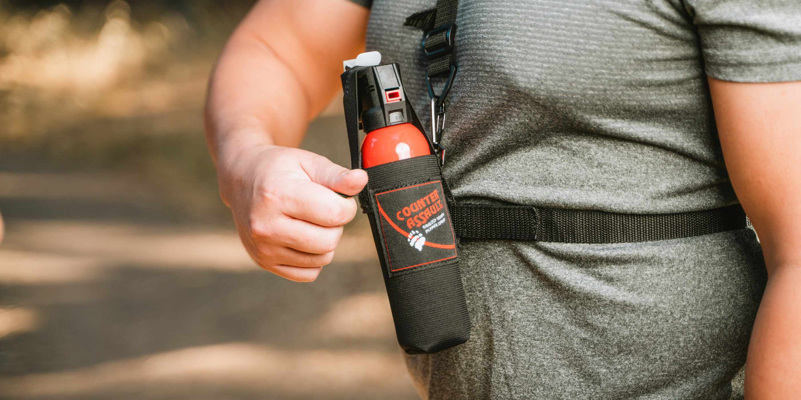 Man in gray shirt attaching Chest Holster with bear spray in it to front of body