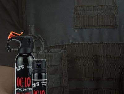 Dark subdued image. Background is the torso of a law enforcement individual wearing a tactical vest, The vest has MOLLE webbing and a radio pouch, with radio, is attached to the webbing. On the left, in front of the radio pouch are the OC10-12 and OC10-4M.