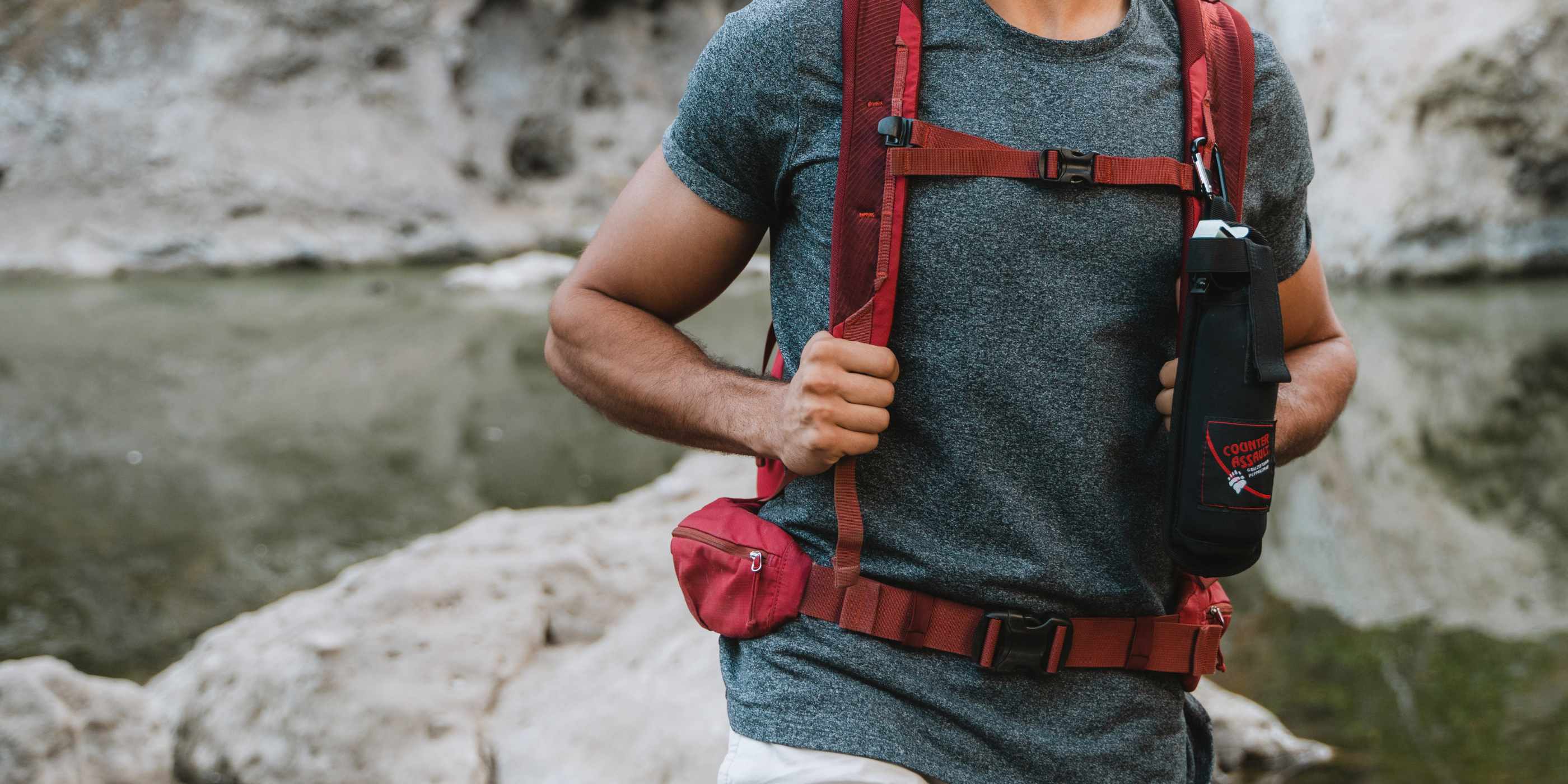 Man with bear spray in Backpack Holster attached to red backpack in front of water