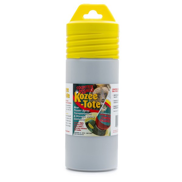 A tall tube container. The lid on top is yellow. The body of this container is gray with a product label. The label has an image of a grizzly bear and another image showing an upside-down bear spray being placed into the container. The label reads as follows: "Counter Assault" as a logo; "Kozee-Tote"; "Bear Pepper Spray Transportation & Storage Safety Container" "Includes: Highly absorbent foam inserts within a heavy-duty container with handle."; "CONFORMS TO: MTDC - 9667-2823"; "USDA Forest Service"