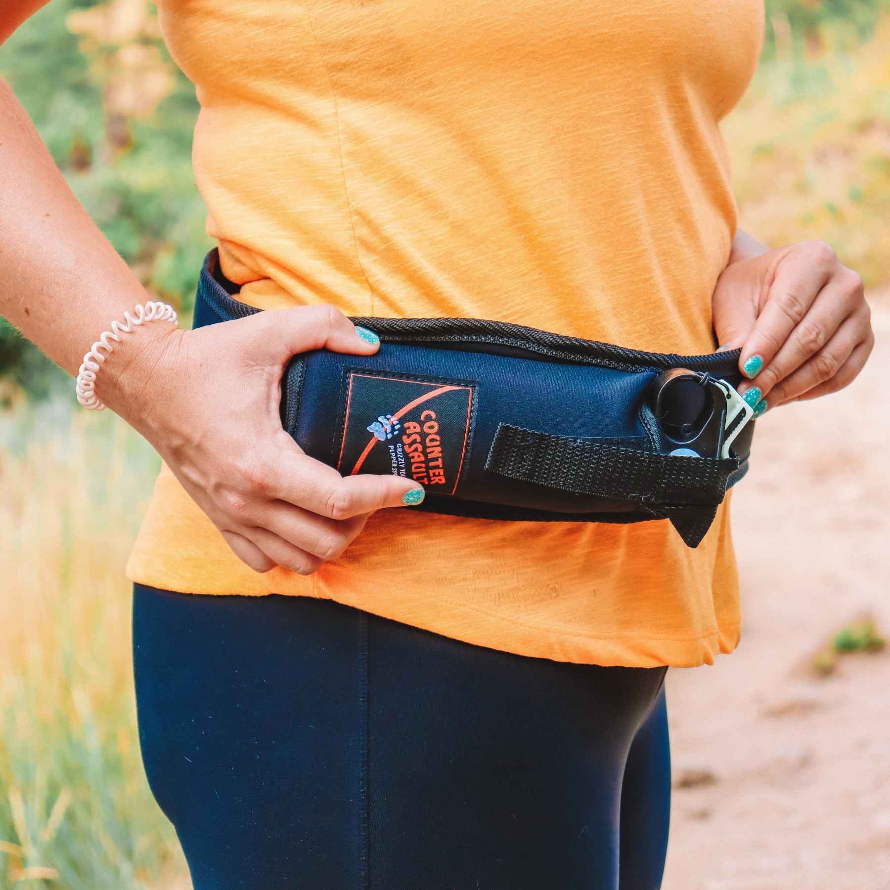 Trail Runner Holster with bear spray attached to the waist of person in orange shirt