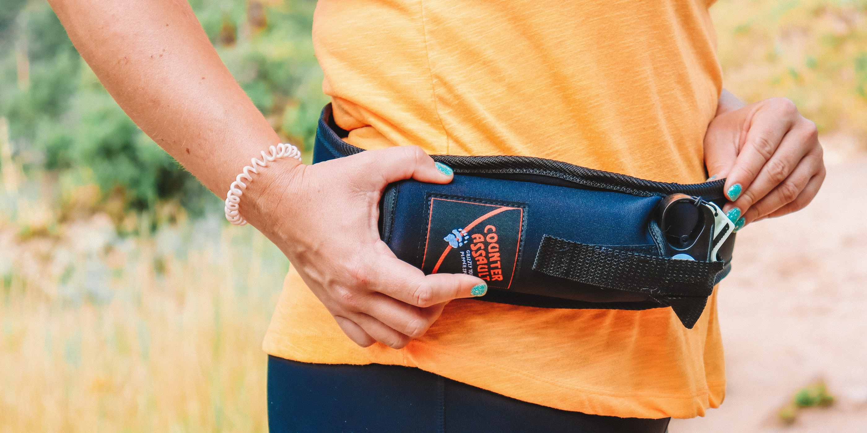 Trail Runner Holster with bear spray attached to the waist of person in orange shirt